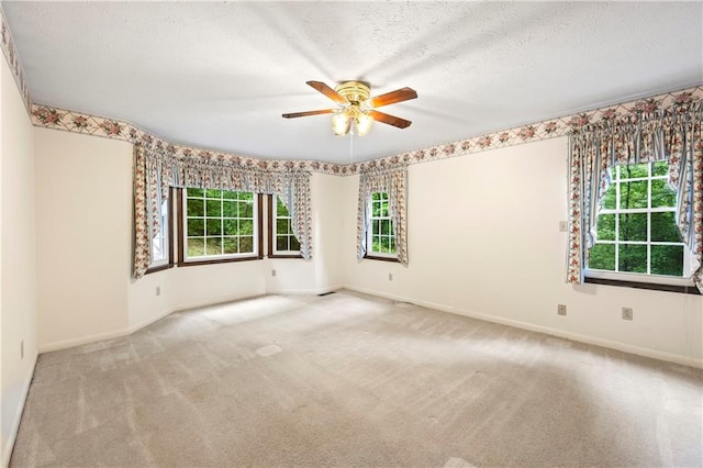 carpeted empty room with a ceiling fan, healthy amount of natural light, a textured ceiling, and baseboards