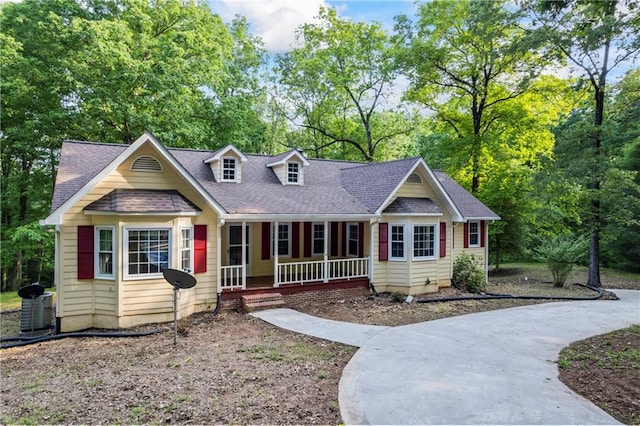 view of front of home featuring covered porch, view of wooded area, roof with shingles, and central AC unit