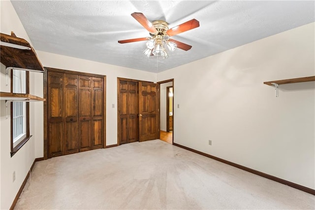 unfurnished bedroom with baseboards, multiple closets, light colored carpet, and ceiling fan