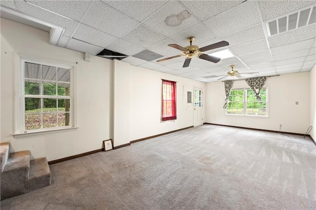 unfurnished living room with a drop ceiling, carpet, baseboards, and a ceiling fan