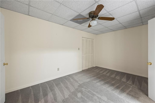 carpeted empty room featuring a paneled ceiling, a ceiling fan, and baseboards