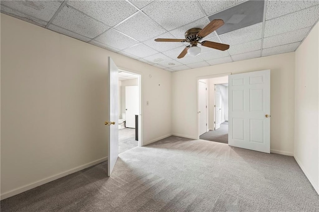 unfurnished bedroom featuring carpet, a drop ceiling, baseboards, and a ceiling fan