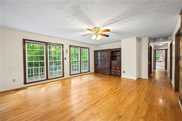 unfurnished living room with light wood-style flooring, a ceiling fan, baseboards, and a textured ceiling