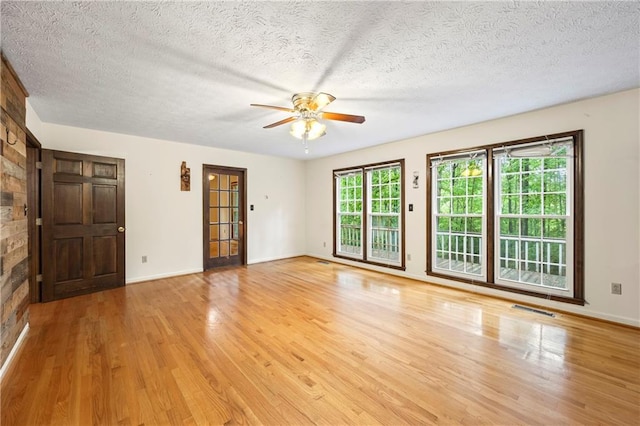 spare room featuring light wood finished floors, a ceiling fan, a textured ceiling, and baseboards