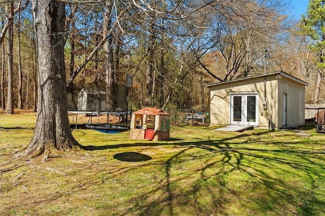 view of yard with french doors, a trampoline, an outdoor structure, and fence