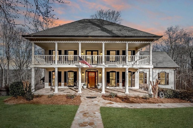 back house at dusk with a yard, a patio, and a balcony