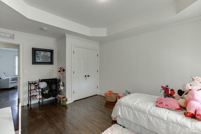 bedroom with a tray ceiling, crown molding, a closet, and dark wood-type flooring