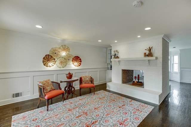 sitting room featuring dark hardwood / wood-style floors, crown molding, and a brick fireplace