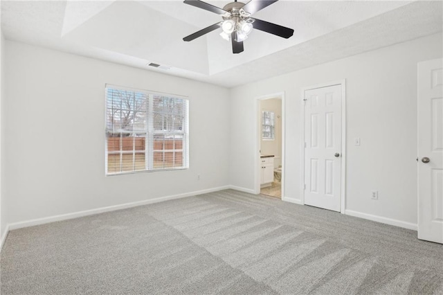 unfurnished bedroom with connected bathroom, a tray ceiling, light colored carpet, and ceiling fan