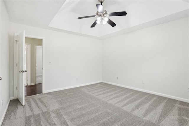 carpeted empty room featuring a raised ceiling and ceiling fan