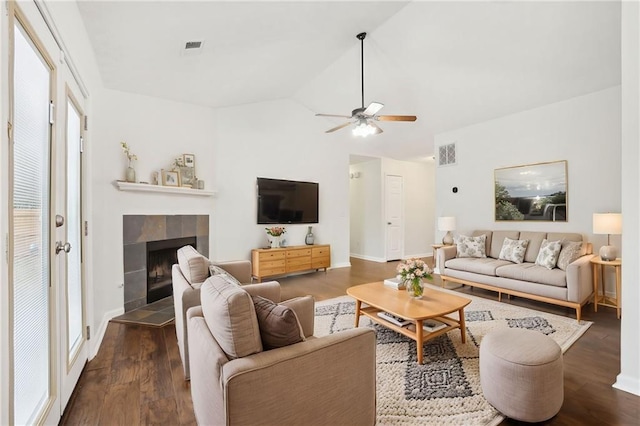 living room featuring dark hardwood / wood-style flooring, a tiled fireplace, vaulted ceiling, and ceiling fan