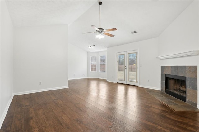 unfurnished living room with dark wood-type flooring, french doors, vaulted ceiling, ceiling fan, and a tiled fireplace