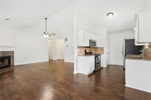 kitchen featuring dark wood-type flooring, a tile fireplace, white cabinetry, dark stone countertops, and stainless steel appliances