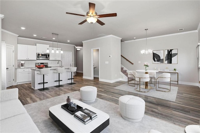 living room with dark wood-type flooring, ornamental molding, ceiling fan with notable chandelier, and sink