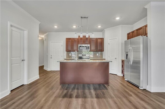 kitchen featuring pendant lighting, backsplash, stainless steel appliances, light stone counters, and an island with sink