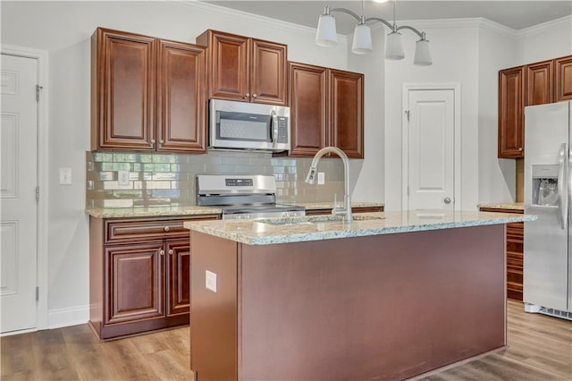 kitchen featuring ornamental molding, appliances with stainless steel finishes, an island with sink, pendant lighting, and light stone countertops