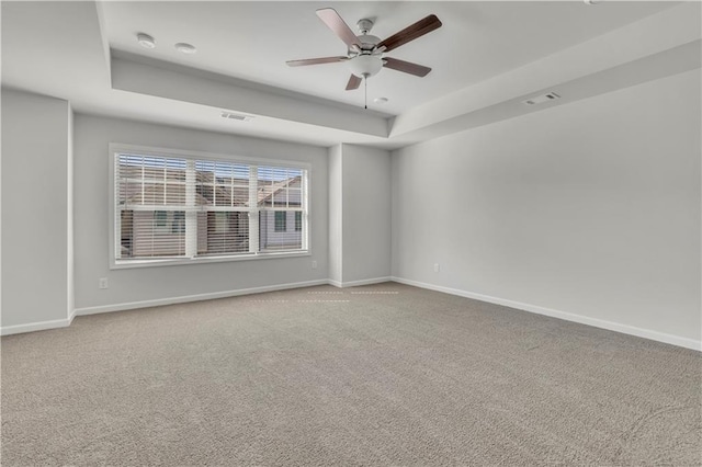 carpeted spare room with a tray ceiling and ceiling fan