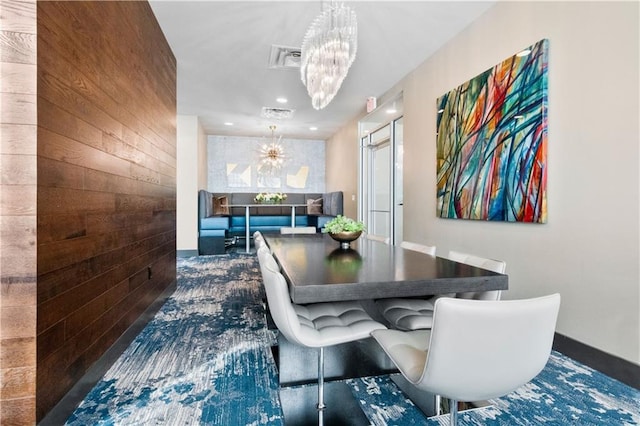 dining area with a chandelier and wood walls