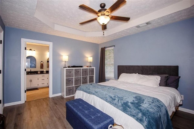 bedroom with dark wood-type flooring, a raised ceiling, a textured ceiling, and ensuite bathroom