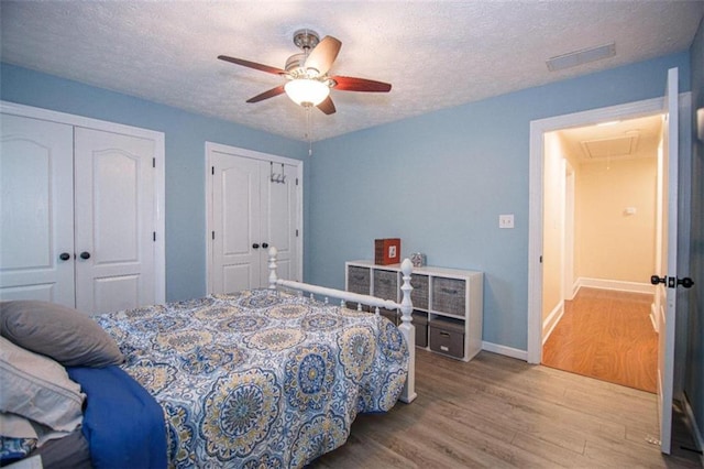 bedroom featuring ceiling fan, two closets, light hardwood / wood-style floors, and a textured ceiling