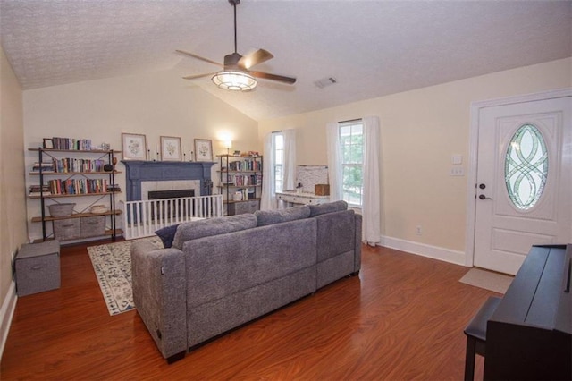 living room featuring a tile fireplace, lofted ceiling, ceiling fan, dark wood-type flooring, and a textured ceiling