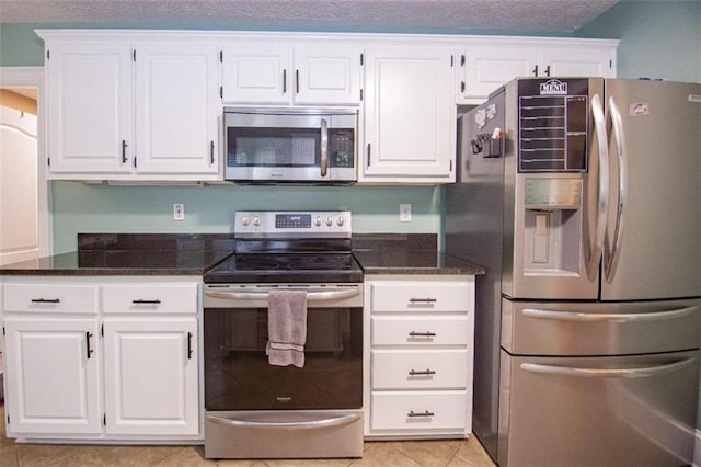 kitchen featuring appliances with stainless steel finishes, dark stone countertops, white cabinets, light tile patterned floors, and a textured ceiling