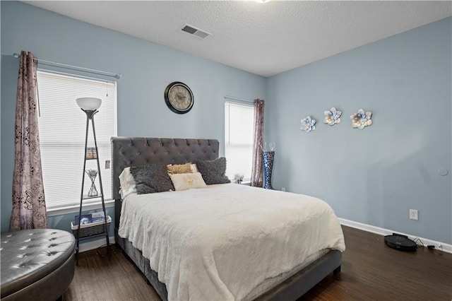 bedroom featuring baseboards, a textured ceiling, visible vents, and wood finished floors