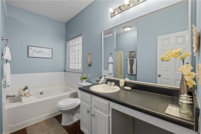 bathroom with a textured ceiling, toilet, wood finished floors, vanity, and a bath