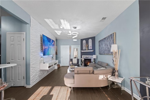 living area with a fireplace, visible vents, a textured ceiling, wood finished floors, and baseboards