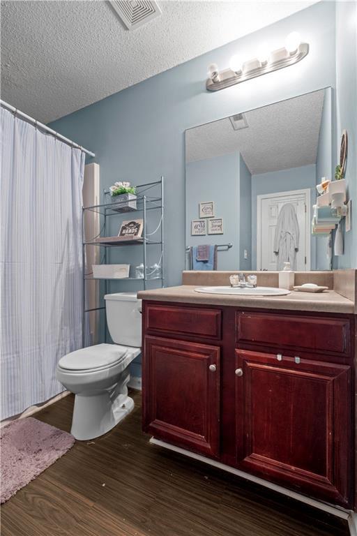 full bath with visible vents, toilet, wood finished floors, a textured ceiling, and vanity