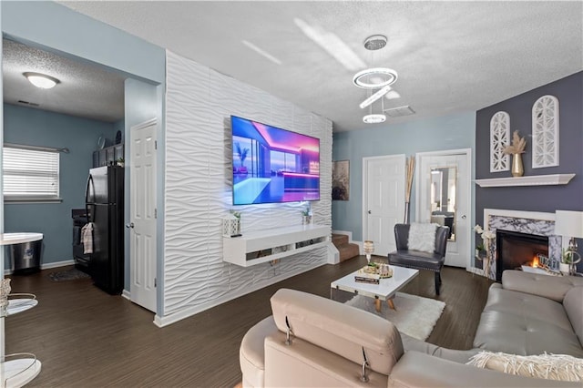 living area with a fireplace, an accent wall, a textured ceiling, wood finished floors, and baseboards