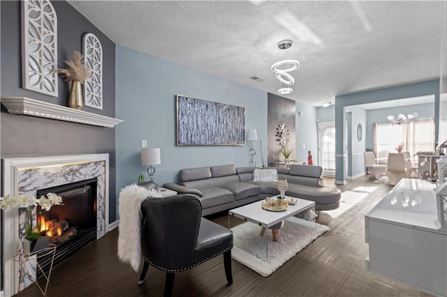 living area with a textured ceiling, a notable chandelier, wood finished floors, a high end fireplace, and baseboards