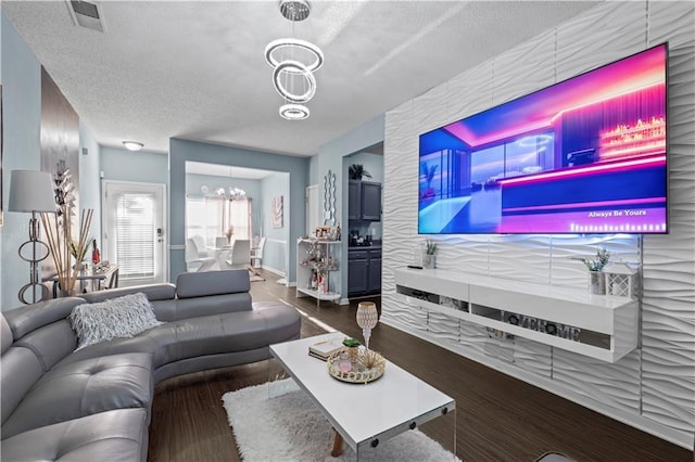 living room with a textured ceiling, visible vents, a notable chandelier, and wood finished floors