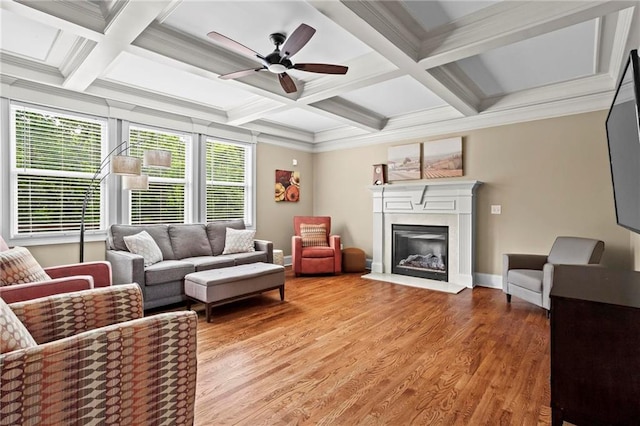 living area with coffered ceiling, baseboards, a glass covered fireplace, ceiling fan, and light wood-type flooring