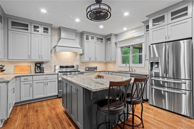 kitchen with appliances with stainless steel finishes, custom exhaust hood, a sink, light wood-style flooring, and gray cabinets