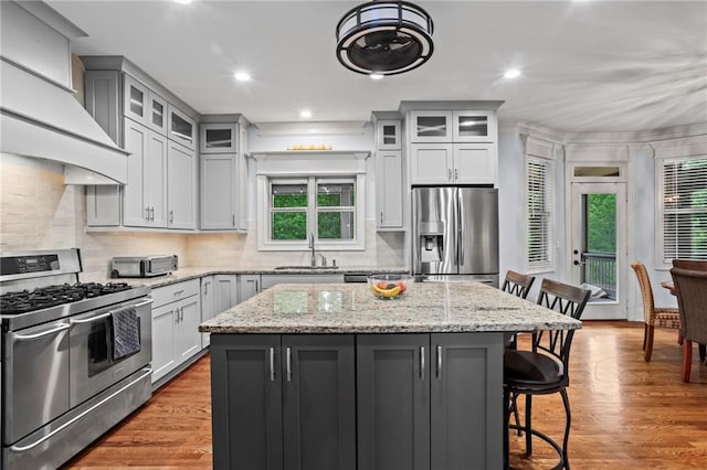 kitchen featuring appliances with stainless steel finishes, a sink, premium range hood, a breakfast bar, and a center island