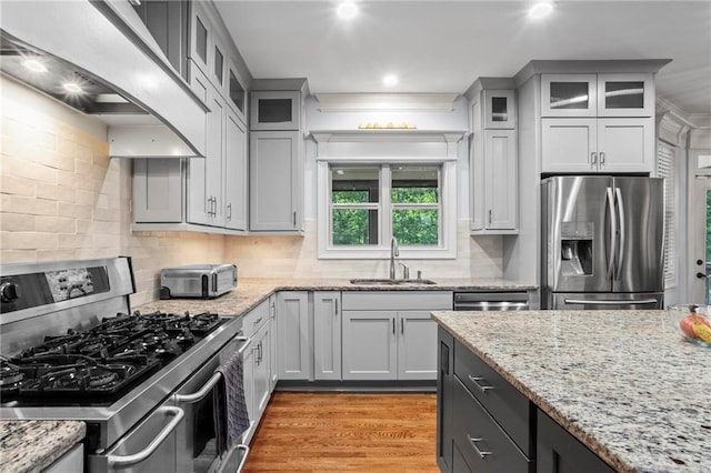 kitchen featuring stainless steel appliances, a sink, wall chimney range hood, decorative backsplash, and light wood-style flooring