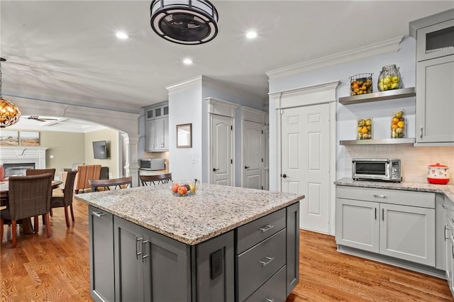 kitchen featuring decorative columns, ornamental molding, arched walkways, gray cabinetry, and open shelves