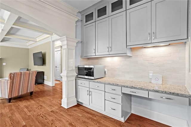 kitchen featuring stainless steel microwave, ornate columns, ornamental molding, light wood-style floors, and backsplash