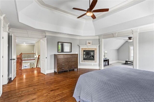 bedroom featuring a tray ceiling, a multi sided fireplace, crown molding, wood finished floors, and baseboards