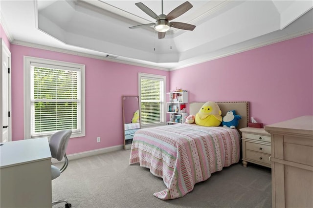 carpeted bedroom featuring a tray ceiling, multiple windows, crown molding, baseboards, and ceiling fan