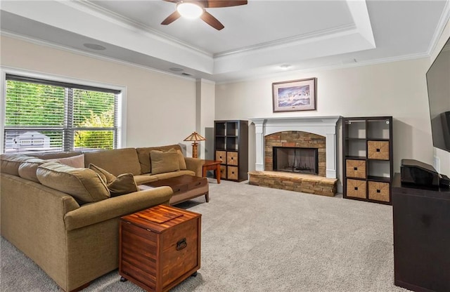 living area featuring carpet, a ceiling fan, crown molding, a raised ceiling, and a stone fireplace