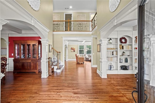 entryway featuring wood finished floors, stairs, arched walkways, a towering ceiling, and crown molding