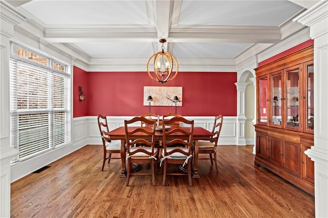 dining area featuring ornate columns, a decorative wall, wood finished floors, crown molding, and coffered ceiling