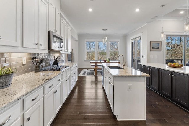 kitchen with pendant lighting, a center island with sink, sink, appliances with stainless steel finishes, and white cabinetry