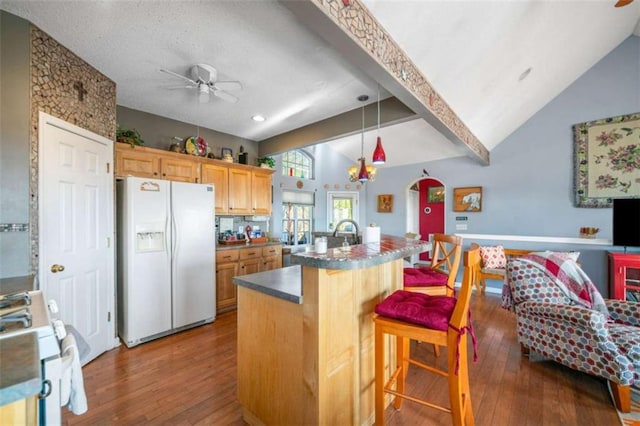 kitchen with white appliances, vaulted ceiling with beams, a kitchen breakfast bar, a center island with sink, and light brown cabinets