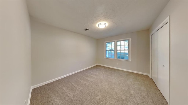 unfurnished bedroom with a closet, light carpet, and a textured ceiling