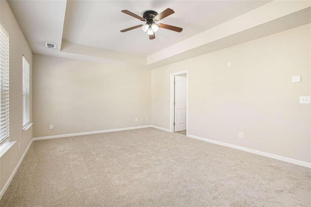 empty room with a raised ceiling, light carpet, and ceiling fan