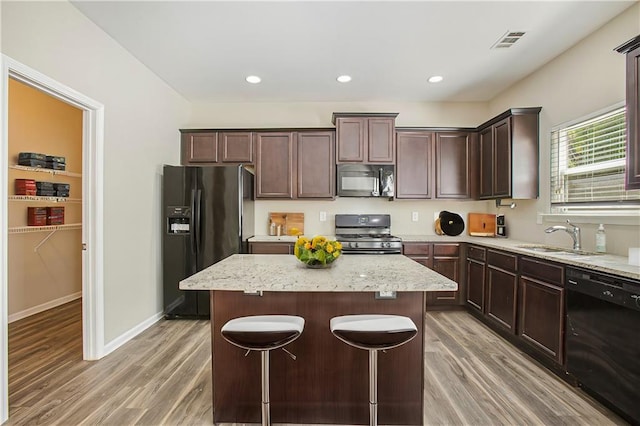 kitchen featuring hardwood / wood-style flooring, sink, black appliances, a center island, and light stone counters