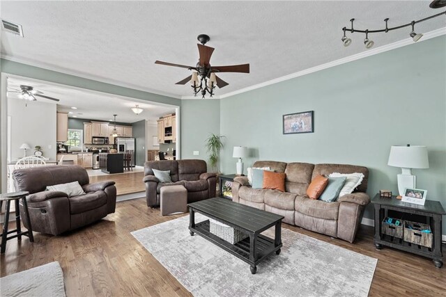 living room featuring ceiling fan, hardwood / wood-style flooring, crown molding, and a textured ceiling